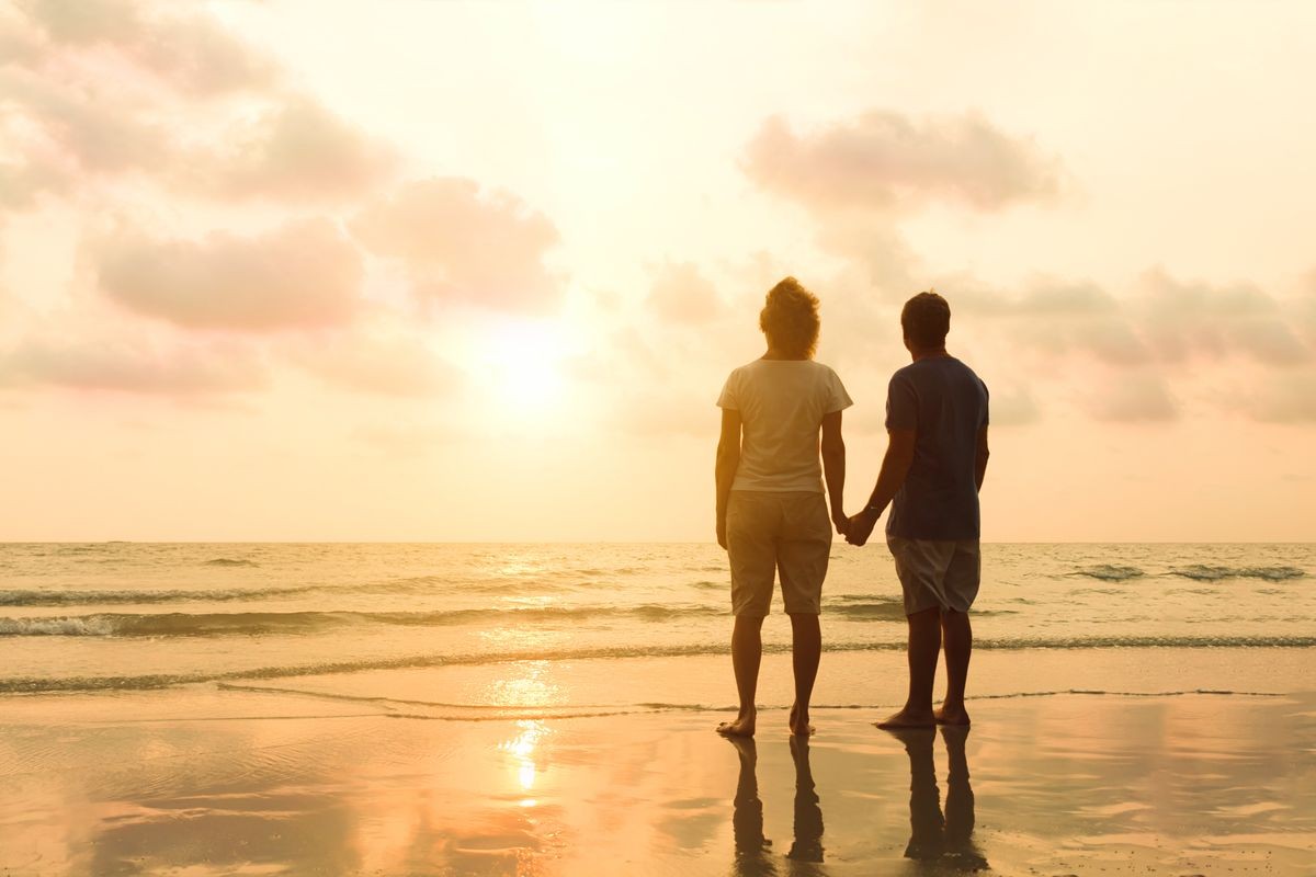 Adult retired couple walking on sunset sea beach and holding hands. Love and romance travel to summer tropical country. Mature relaxation and happiness leisure